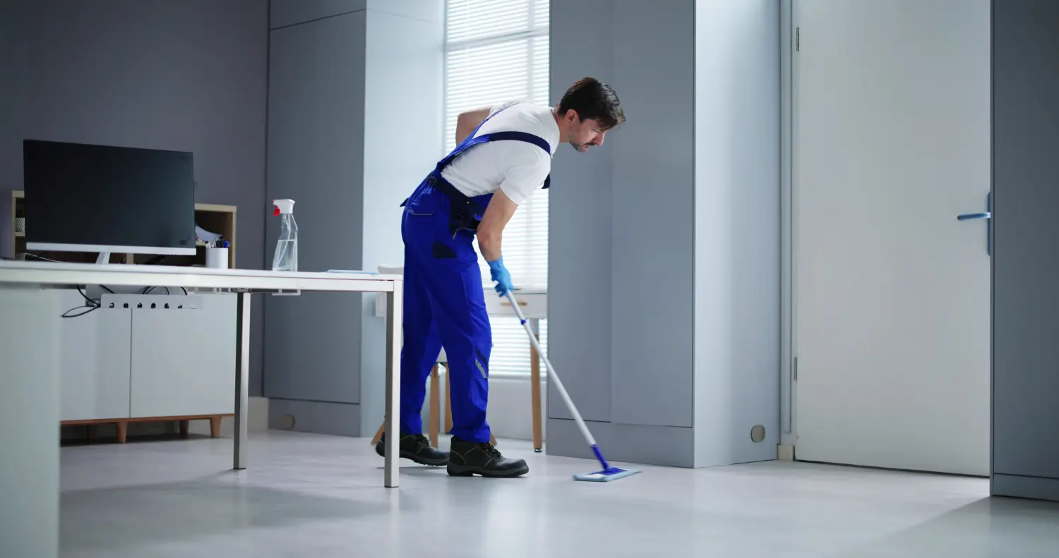 Porträt eines glücklichen männlichen Hausmeisters, der den Boden im Büro reinigt